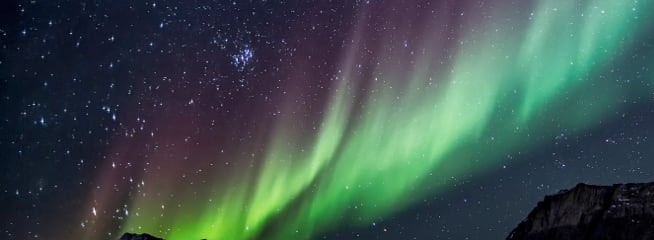 View of Aurora Borealis lights in the night sky over mountains.